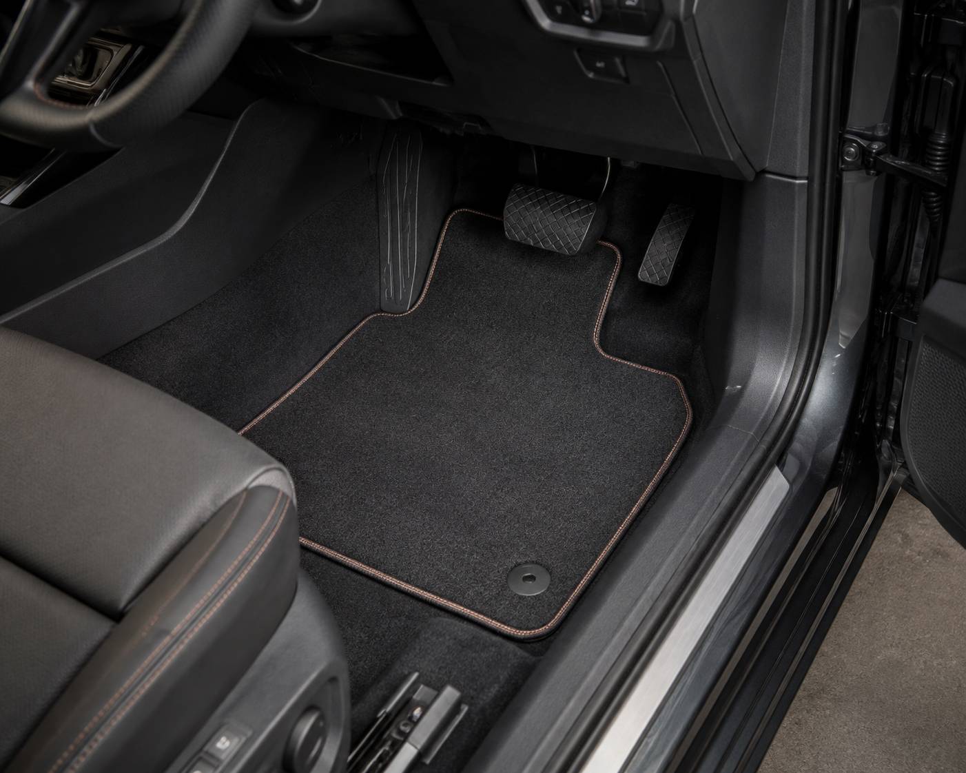 Tailored charcoal car mat with contrast stitching, fitted in a vehicle footwell over the original fixing point
