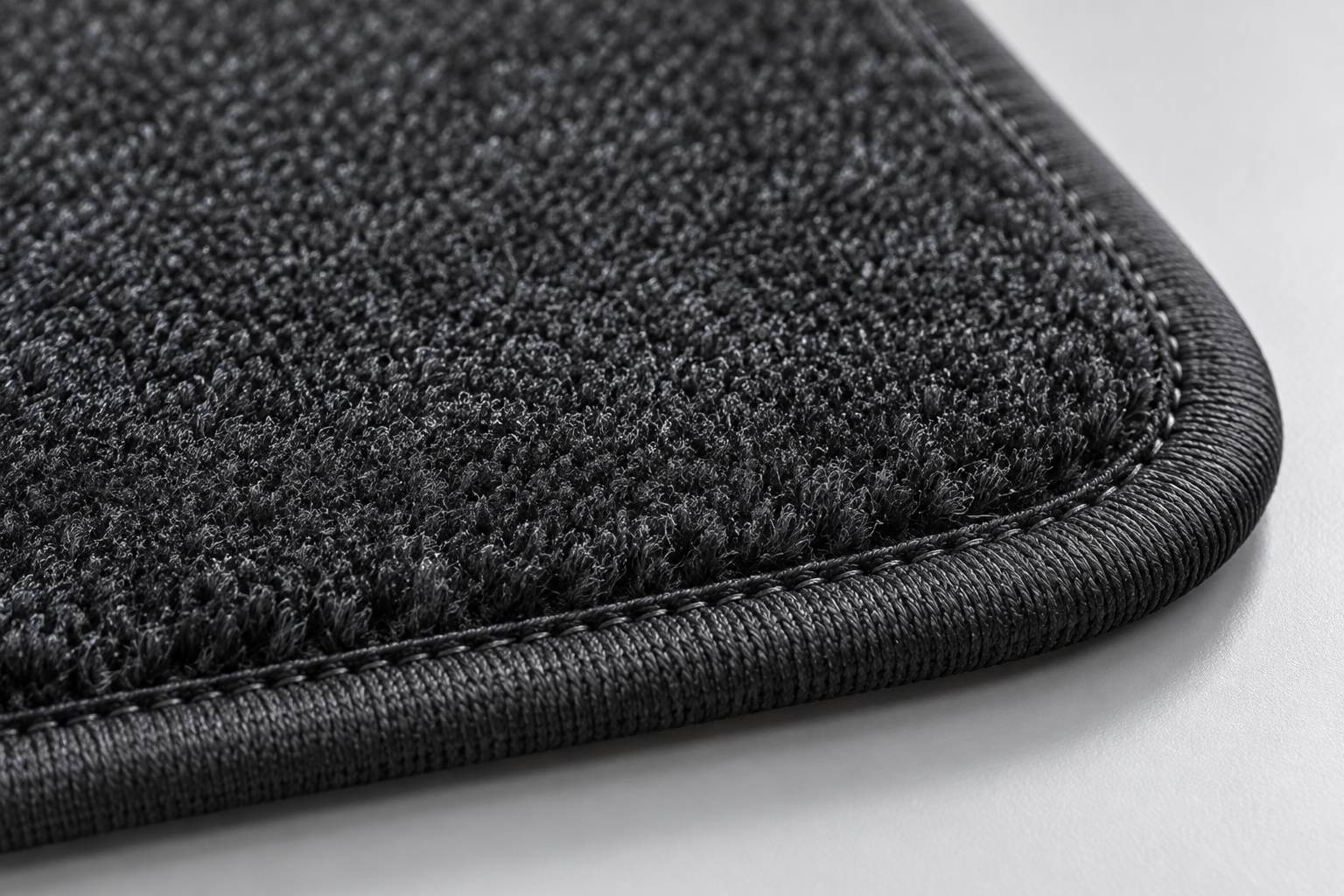 Macro view of the corner of a charcoal carpet mat showing the pile depth and the bound edge with its stitching