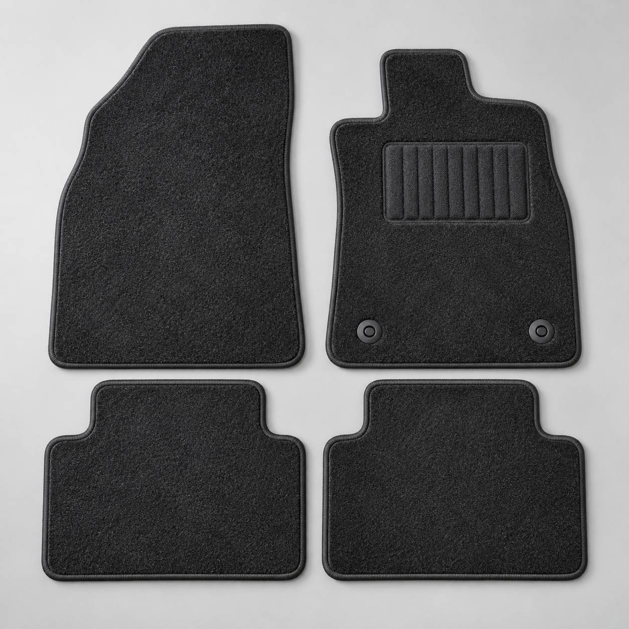 A four piece charcoal carpet mat set laid out flat, driver mat with a reinforced heel pad and two fixing clips